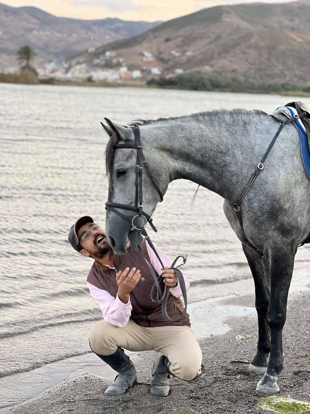 Un homme serrant contre lui son cheval gris, au bord de l'eau